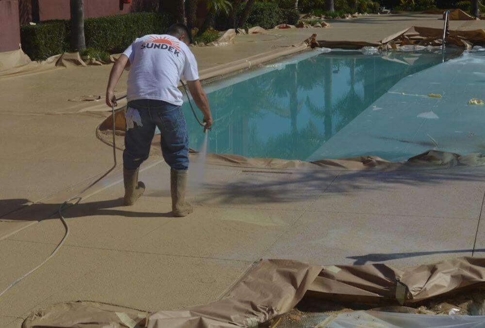 Sundek installer using spray knockdown texture to resurface pool