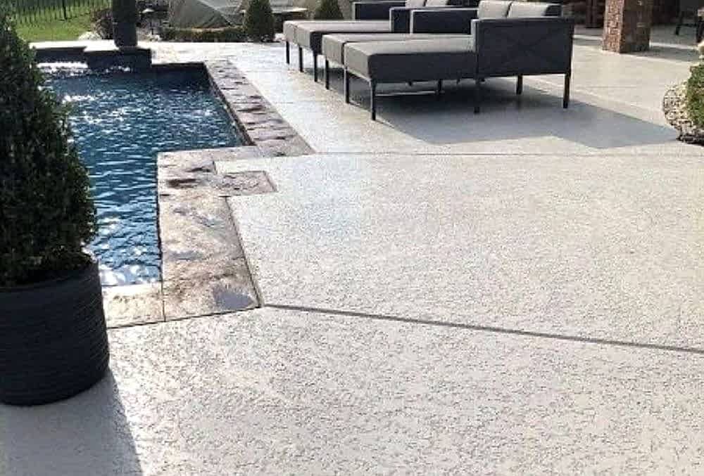 Textured pool deck with a wide outdoor couch beside the swimming pool, creating a relaxing and stylish lounging area.